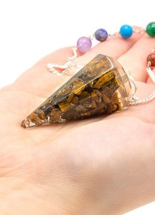 Péndulo de orgonita de ojo de tigre con 7 chakras sostenido en la mano para radiestesia y armonización energética